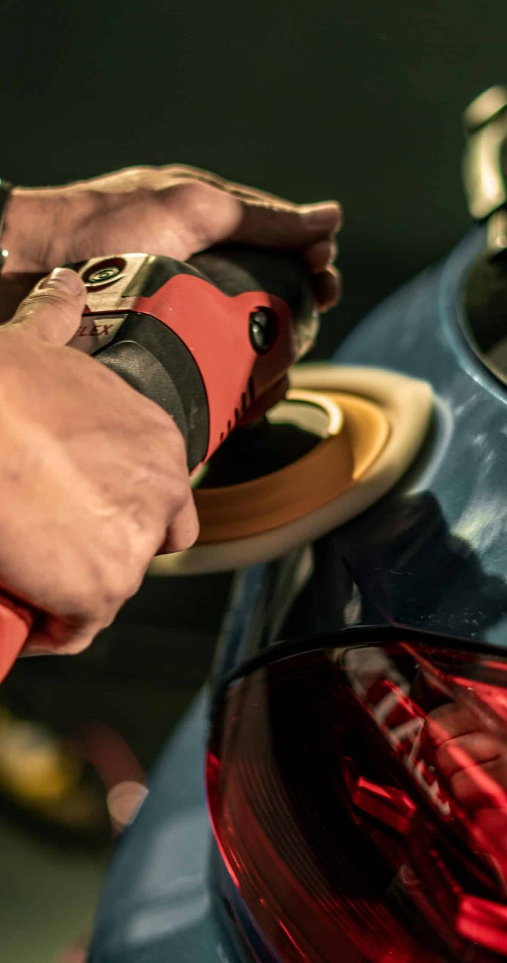 Hands using a buffing machine to polish a car for a glossy finish, highlighting car detailing process.